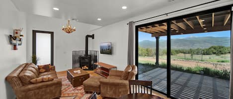 A modern living room with a fireplace, leather sofas, a wooden coffee table, and a large sliding glass door leading to a patio with a mountain view.