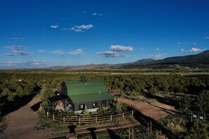 A house with a green roof, surrounded by a wooden fence, set in a rural landscape with mountains in the background. - The King Ranch I South Fork, Colorado Retreat (South Fork)