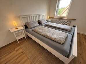 A bedroom with a bed, bedside tables, a lamp, a window, and a radiator. - "Anna" Vacation Home - Heideglück Apartment on the First Floor - Centrally Located! (Winsen (Aller))
