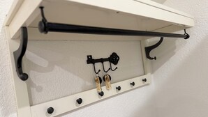 Ein weißes Regal mit Haken und einer schwarzen Stange, vermutlich zum Aufhängen von Gegenständen.