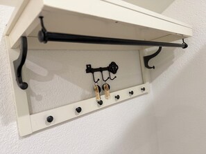 Ein weißes Regal mit Haken und einer schwarzen Stange, vermutlich zum Aufhängen von Gegenständen.