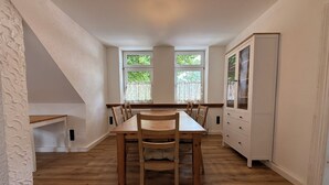 Ein Essbereich mit einem Holztisch und Stühlen, einem weißen Schrank und zwei mit Vorhängen versehenen Fenstern.