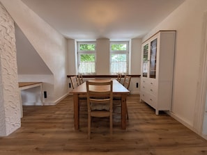 Ein Essbereich mit einem Holztisch und Stühlen, einem weißen Schrank und zwei mit Vorhängen versehenen Fenstern.