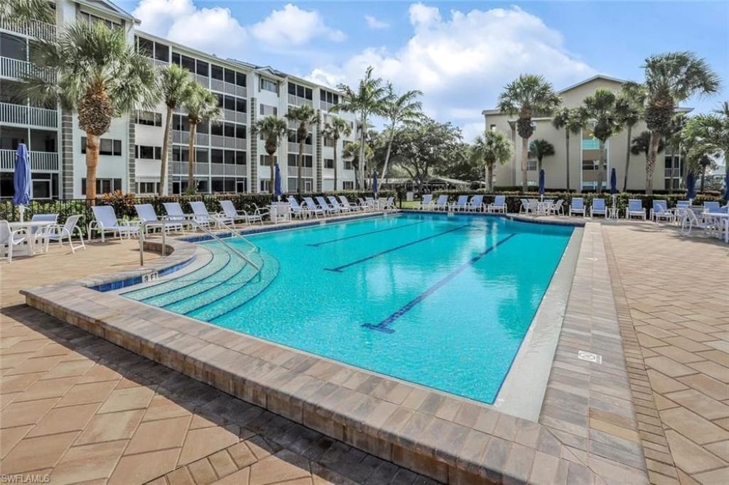 A swimming pool with lounge chairs, palm trees, and a building with multiple floors.