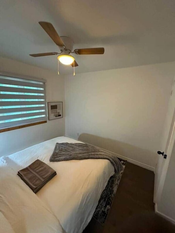 A bedroom with a bed, a ceiling fan, a window with blinds, and a door. - Logement au centre Ville de Québec (Québec City)