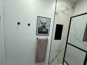 A bathroom with a marble wall, a framed picture of a bull, a towel rack, and a black electrical outlet. - Logement au centre Ville de Québec (Québec City)