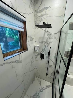 A bathroom with marble walls, a window, a shower, and a glass enclosure. - Logement au centre Ville de Québec (Québec City)
