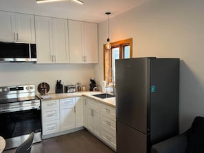 A modern kitchen with white cabinets, a stainless steel oven, a black refrigerator, and a wooden countertop. - Logement au centre Ville de Québec (Québec City)