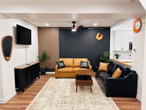 Ein modernes Wohnzimmer mit einer Sofagarnitur, einem Couchtisch, einem Fernseher und einem Deckenventilator.