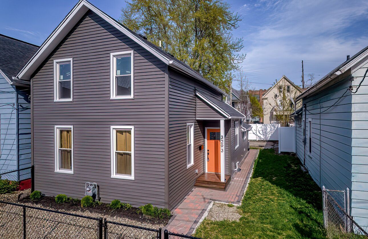 A two-story residential house with a front porch, a visible garage door, and a small front yard.