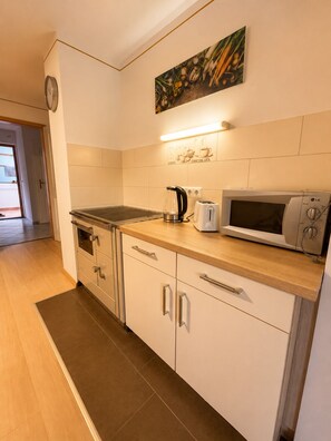 A modern kitchen with a microwave, toaster, kettle, and a clock on the wall.