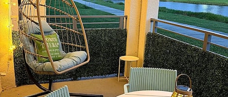 Un patio con una mesa redonda, dos sillas, una silla colgante y vistas a un cuerpo de agua.