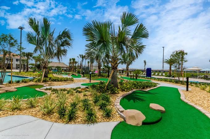 A golf course with a putting green, palm trees, and a pool area.