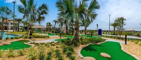A golf course with a putting green, palm trees, and a pool area.