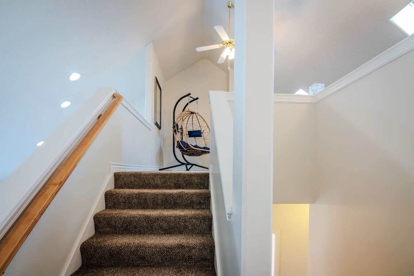A staircase with carpeted steps, a ceiling fan, and a hanging chair.