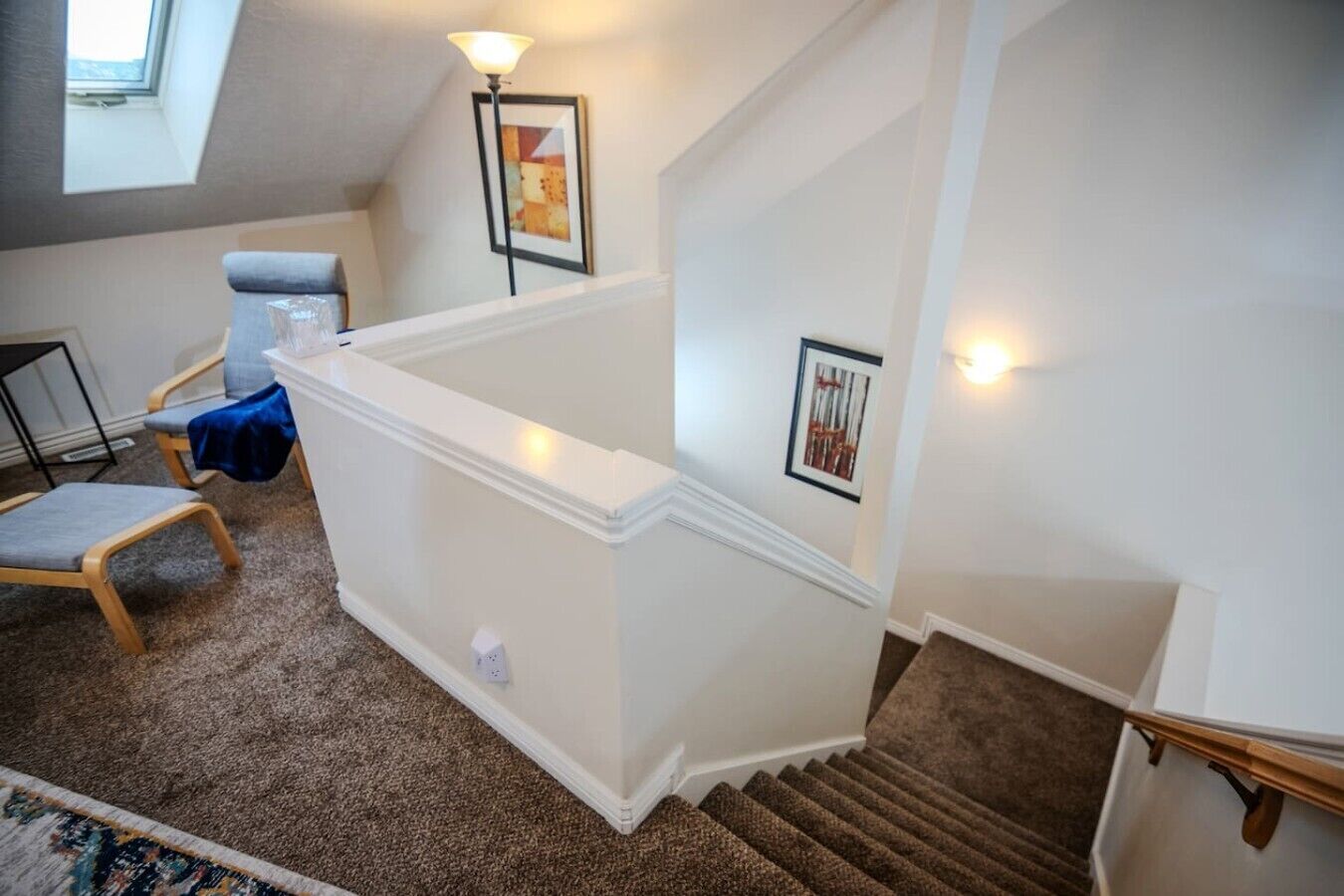 A staircase with a carpeted landing, a chair, a desk, and framed artwork on the walls.