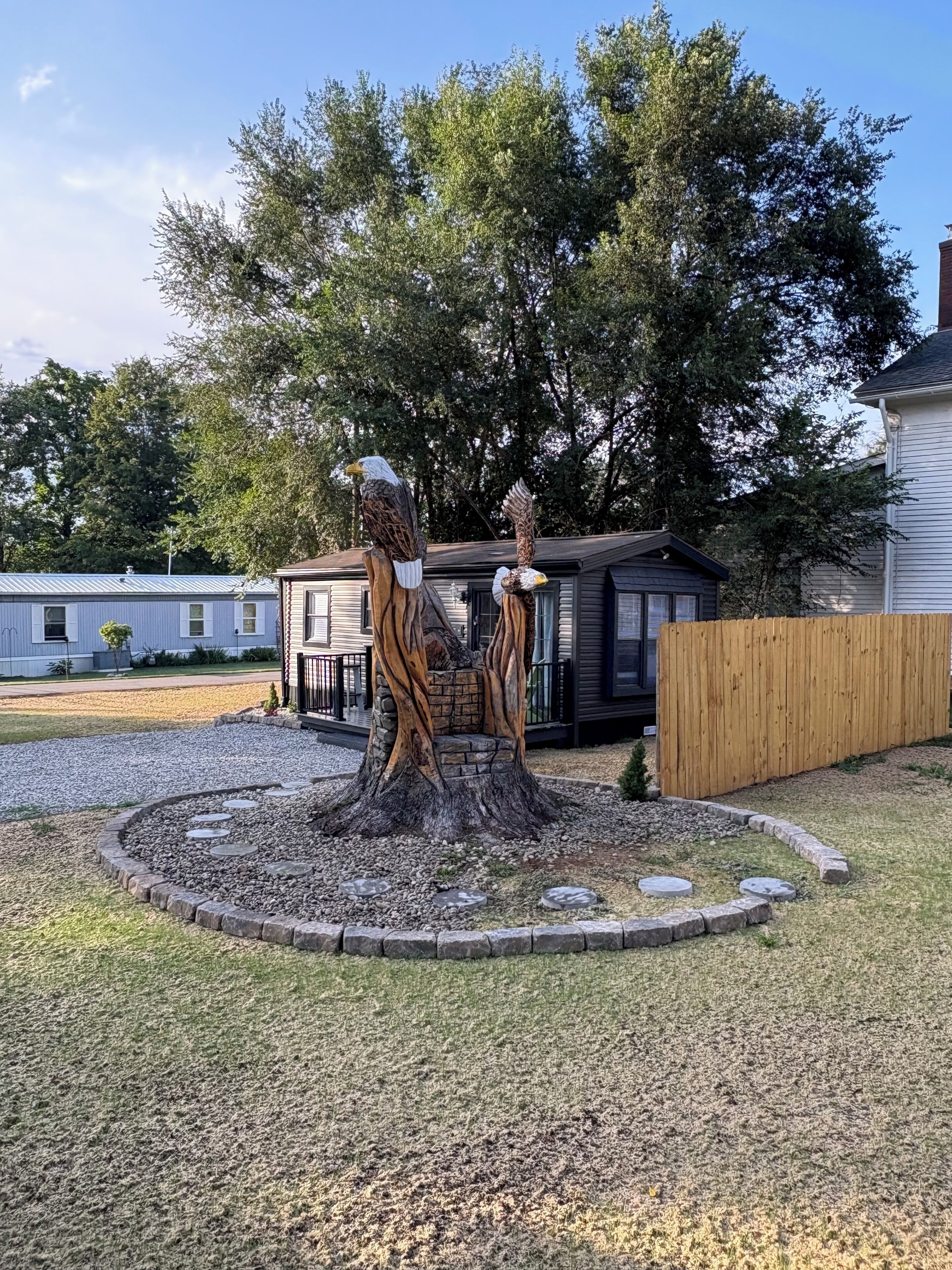 A wooden sculpture of two eagles perched on a tree stump with a circular stone pathway around it.