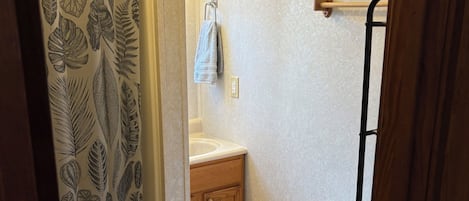 Ein Badezimmer mit Duschvorhang mit Blättermotiv, einem Holzkabinent, einer Toilette und einem Handtuchhalter.