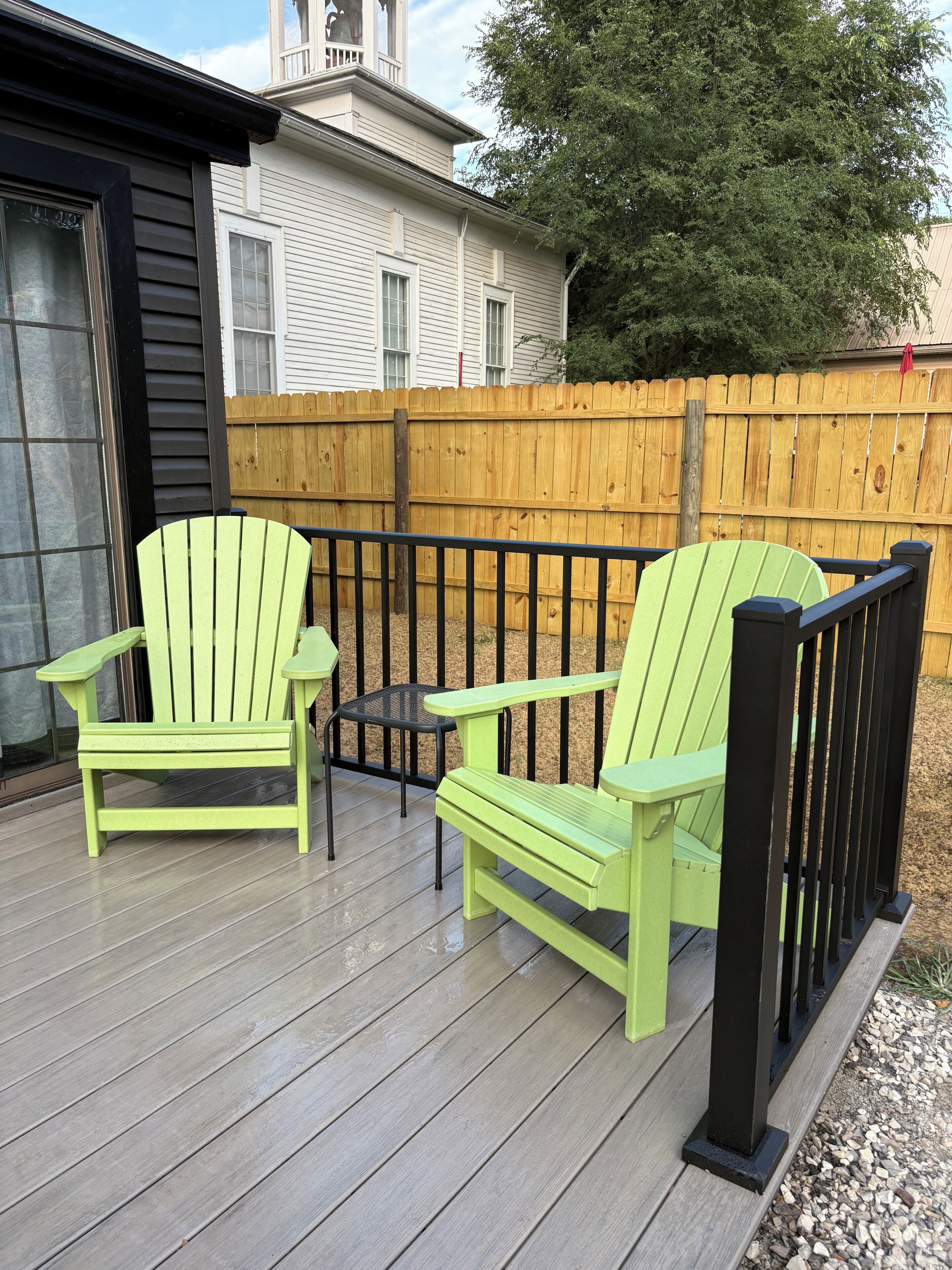 A wooden deck with two green Adirondack chairs and a small table.