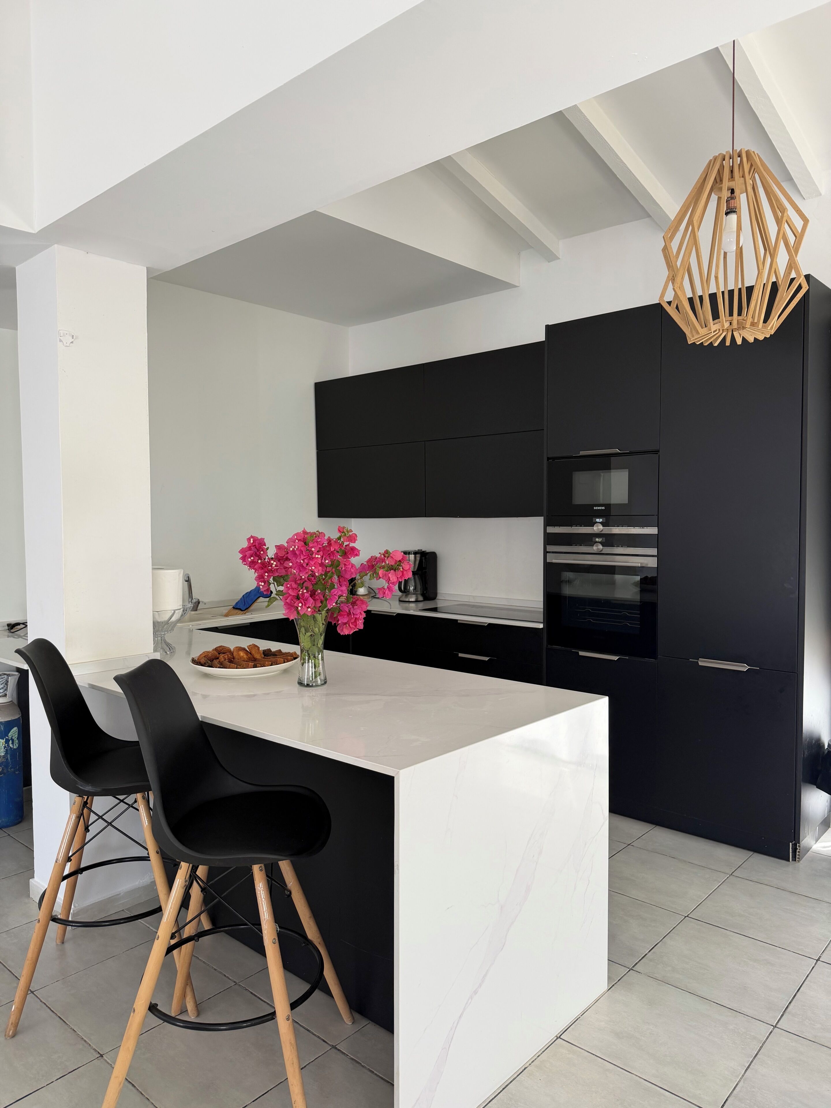 Una cucina moderna con isola centrale, pensili neri e lampada a sospensione.
