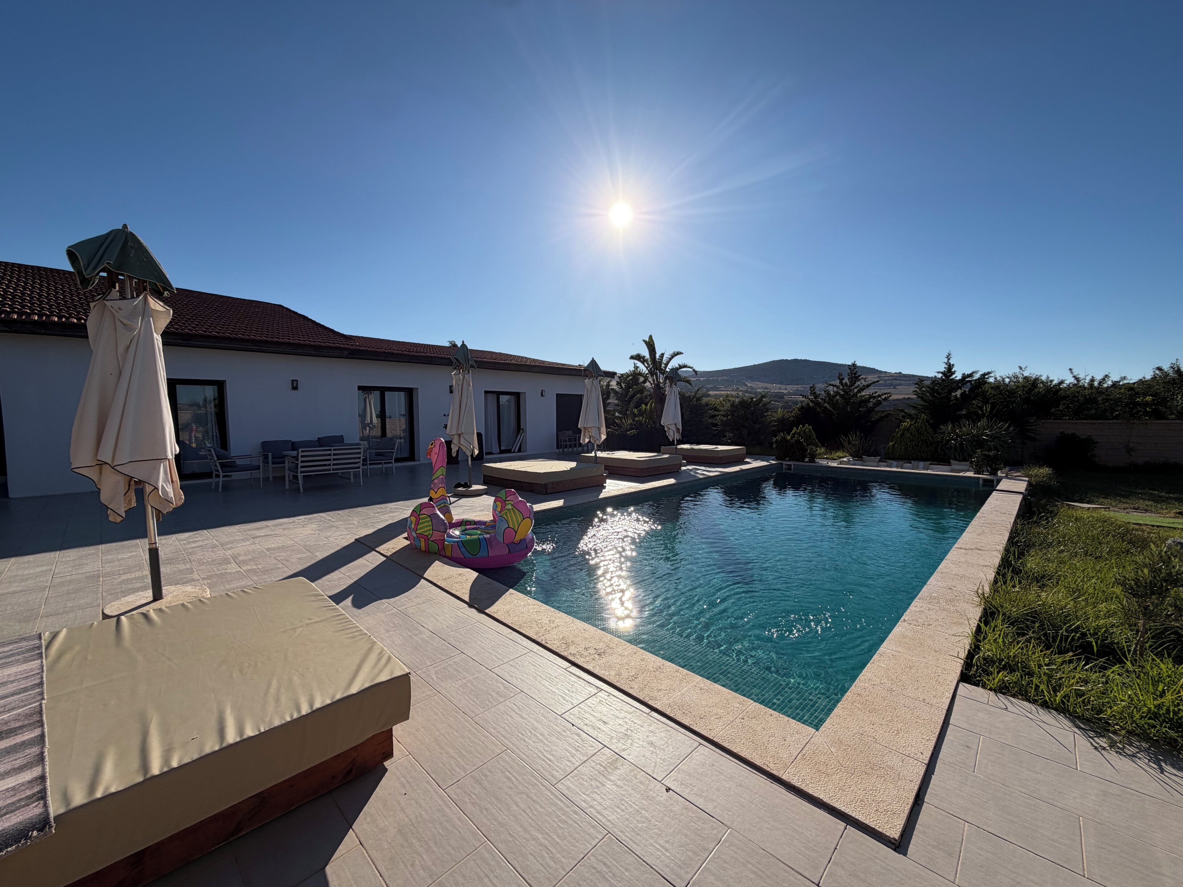 Una piscina con cielo luminoso, posti a sedere all'aperto e vista su una collina.