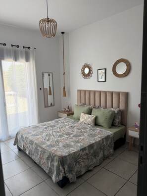A bedroom with a bed, a bedside table, a hanging light fixture, a mirror, and a window with curtains.