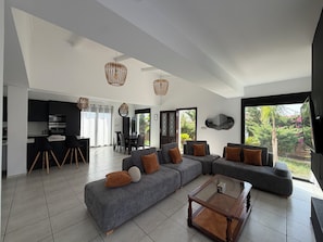 A modern living room with a sectional sofa, a glass coffee table, and a dining area with chairs and a table.