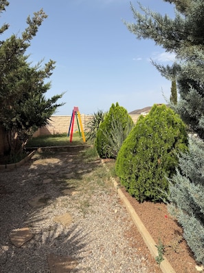 A garden with a gravel path, a colorful swing set, and various shrubs.