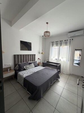 A modern bedroom with a large bed, a bedside table, a hanging light fixture, and a window with curtains.