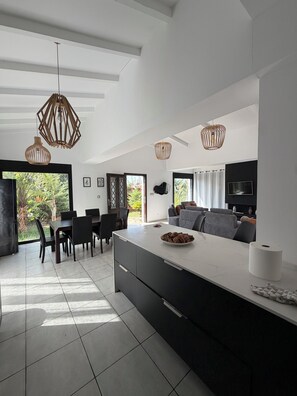 A modern kitchen with a central island, dining area, and a living space with a TV.