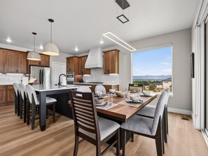 A modern kitchen with wooden cabinets, a central island, and a dining area with chairs and a table. - NEW! Mesa View Modern: Luxury Living (Grand Junction)