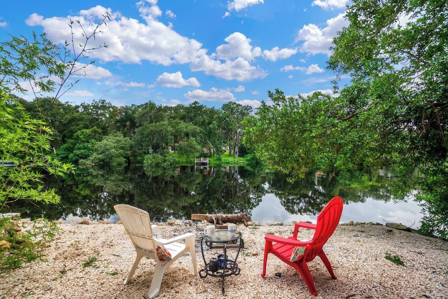 Two chairs facing a calm lake with a clear sky.