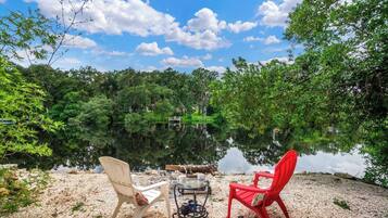 Two chairs facing a calm lake with a clear sky.