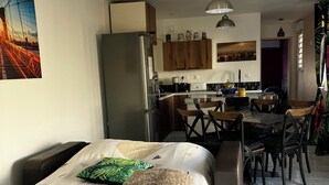 A compact living space with a bed, a dining area, a kitchen, and a large window. - Small vacation rental near the beaches (Triaize)