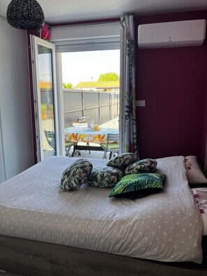 A bedroom with a bed, pillows, a window, and an air conditioning unit. - Small vacation rental near the beaches (Triaize)