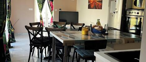 A modern kitchen with a dining area, featuring a large island, stainless steel appliances, and pendant lighting.