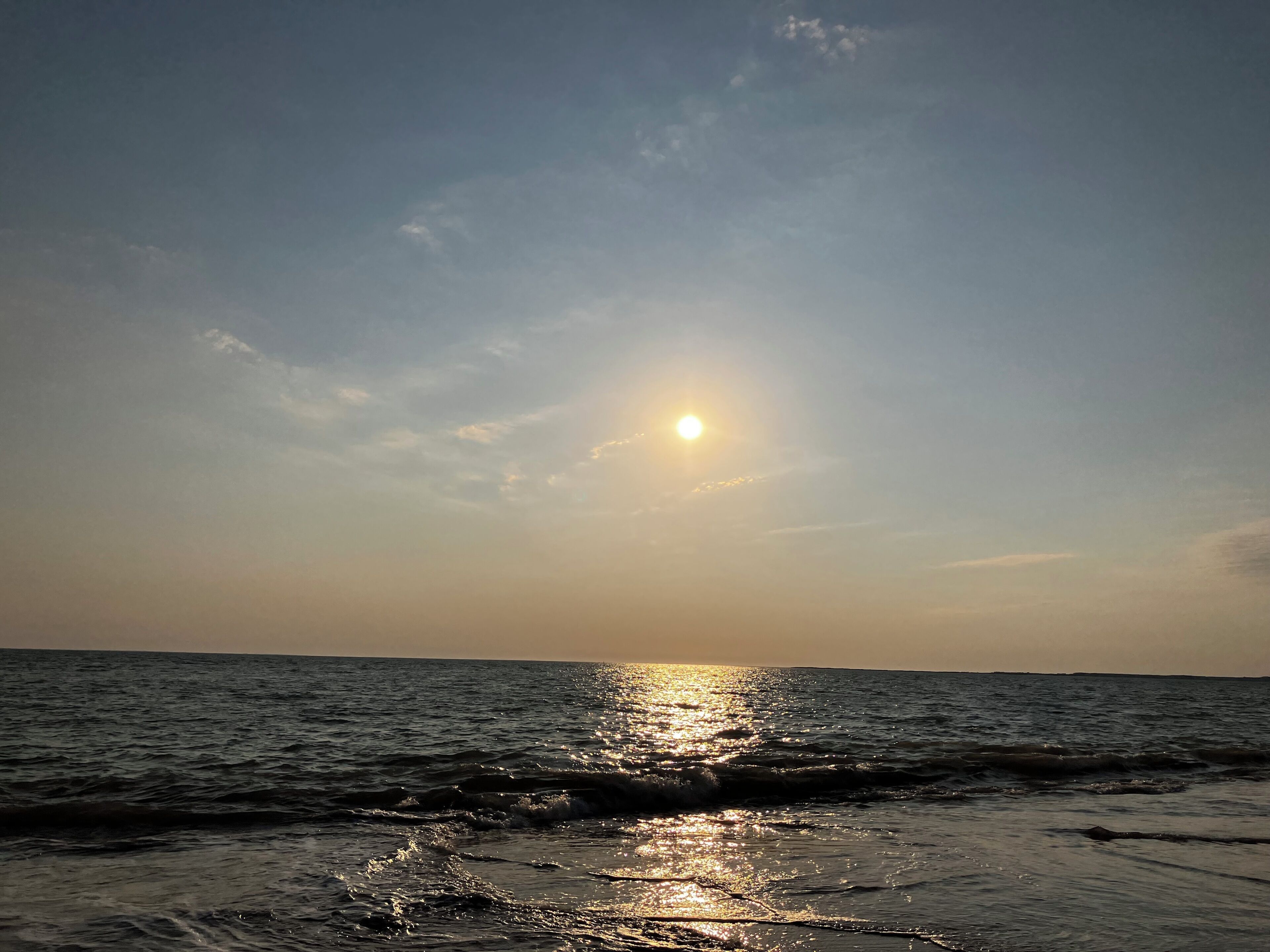 Ein Sonnenuntergang über dem Meer, wobei Wellen das Sonnenlicht reflektieren.