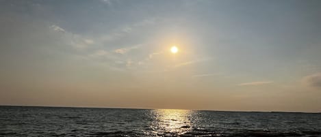 A sunset over the ocean with waves reflecting the sunlight.