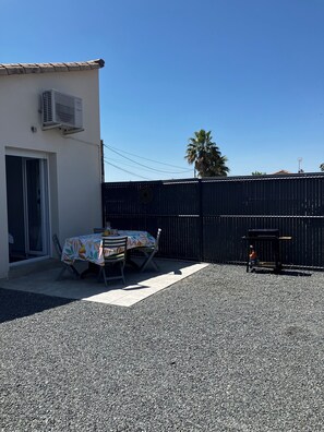 A patio area with a table and chairs, a black fence, and an air conditioning unit on a building. - Small vacation rental near the beaches (Triaize)