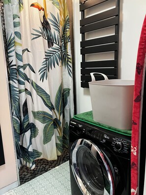 A laundry area with a washing machine, a drying rack, and a curtain with a tropical leaf pattern. - Small vacation rental near the beaches (Triaize)