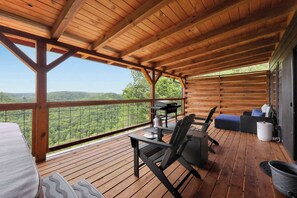A wooden deck with a table and chairs, a grill, and a view of the forest. - Sugar Maple Cabin - Romantic, Sauna, View, Hot Tub (Rogers)
