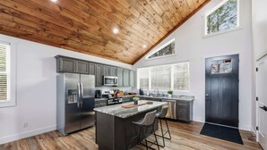 A modern kitchen with a wooden ceiling, stainless steel appliances, and a central island with bar stools. - Sugar Maple Cabin - Romantic, Sauna, View, Hot Tub (Rogers)