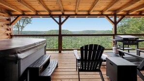 A covered outdoor deck with a grill, seating, and a view of the surrounding landscape. - Sugar Maple Cabin - Romantic, Sauna, View, Hot Tub (Rogers)