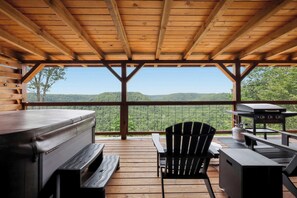 Eine überdachte Terrasse im Freien mit Grill, Sitzgelegenheiten und Blick auf die umliegende Landschaft.