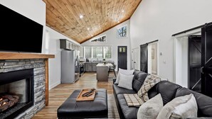 A spacious living area with a fireplace, a black leather sofa, and a wooden ceiling. - Sugar Maple Cabin - Romantic, Sauna, View, Hot Tub (Rogers)