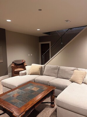 A modern living room with a sectional sofa, a wooden coffee table, and a staircase.