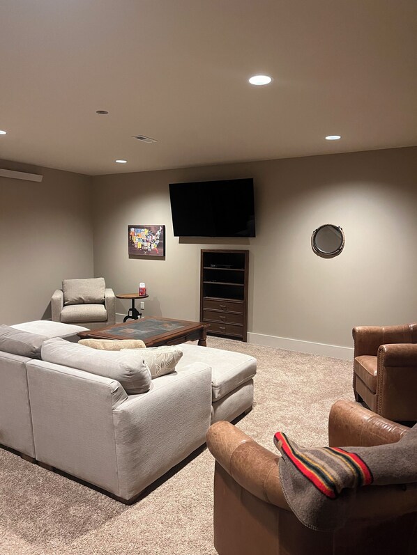 A living room with a sectional sofa, a recliner, a coffee table, a flat-screen TV, a small table with a lamp, and a wall-mounted mirror.