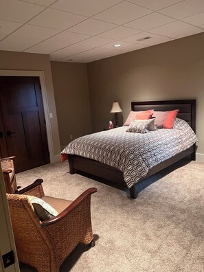 A bedroom with a bed, a chair, a lamp, and a door.