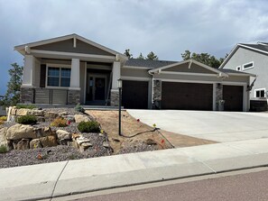 A modern two-story house with a stone facade, a garage, and a landscaped front yard. - USAFA Retreat, 4BR/ 4BA, Front Range Views, Nestled in the Pines (Monument)