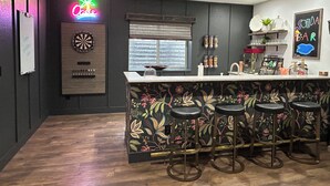 A bar area with a dartboard, bar stools, and a neon sign. - USAFA Retreat, 4BR/ 4BA, Front Range Views, Nestled in the Pines (Monument)
